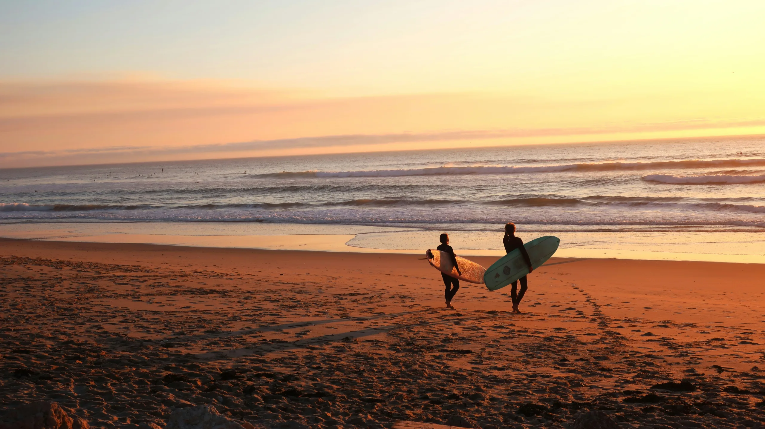 duas pessoas caminhando na praia em direção ao mar durante o por do sol